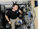 Floating in microgravity, ISS Expedition 25 Commander Doug Wheelock, KF5BOC, speaks to Earth via ham radio from NA1SS. The transceiver control head is just visible on the cluttered bulkhead, with operating instructions posted conveniently adjacent. All gear is secured, so it doesn’t float around the cabin. [NASA Photo]